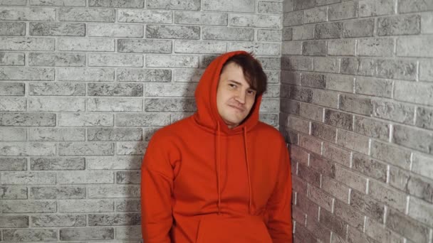 Un beau jeune homme dans un hoodie rouge hoche la tête en signe d'approbation sur un fond de brique. Un brunet fait un geste d'accord. — Video