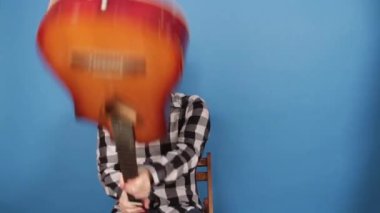 Deli bir adam gitarla kendi kafasına vurur. Adam mavi arka planda kafasında bir gitar kırıyor..