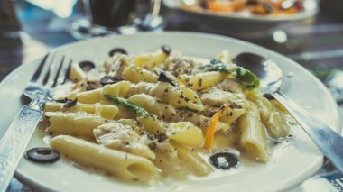 Beyaz soslu makarna, deniz ürünleri, beyaz tabak ve çatal bıçak.