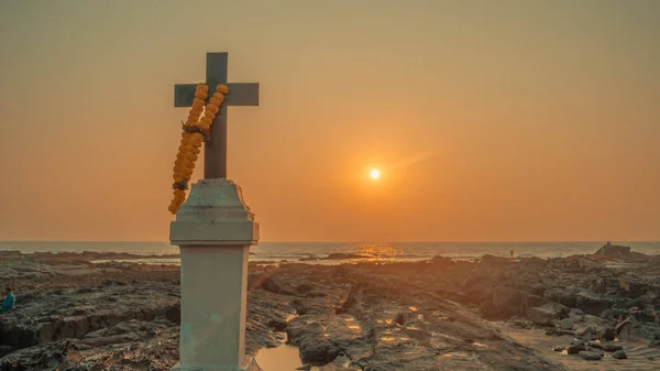 A cruz cristã nas rochas junto ao mar contra o pôr-do-sol . — Fotografia de Stock