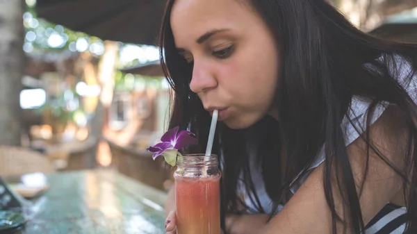 Krásná mladá žena pije zdravý pomerančový smoothie v tropické kavárně.Krásná dívka pije čerstvý džus nebo koktejl. — Stock fotografie