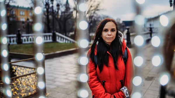 Ritratto di una bella giovane donna in giacca e cappuccio attraverso una ghirlanda per strada. — Foto Stock