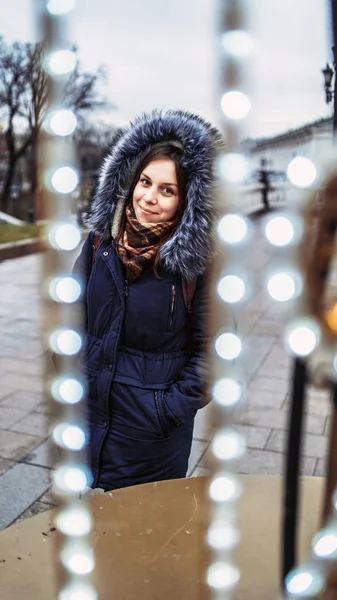 Egy gyönyörű fiatal nő portréja kabátban és kapucniban egy koszorúban az utcán.. — Stock Fotó