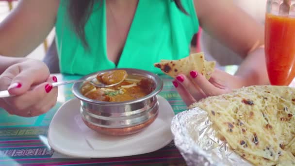 Een jonge vrouw eet een Indiaas vleesgerecht in een tropisch café. — Stockvideo