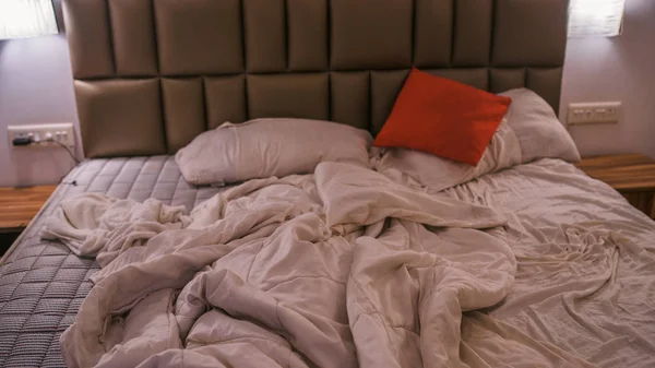 Пустая измятая кровать в отеле. Смятое одеяло и подушки. Крупный план грязной кровати. Постельное белье, простыни и подушки после сна ночью . — стоковое фото