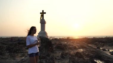 Güzel genç bir kadın Hristiyan haçı yakınındaki bir şişeden gün batımına karşı soğuk bir su içiyor..