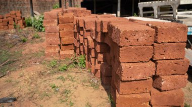 Bahçede yığınla tuğla var. Güneşli bir günde kumlu zeminde çimlerle kaplı eski püskü kırmızı tuğlalar.