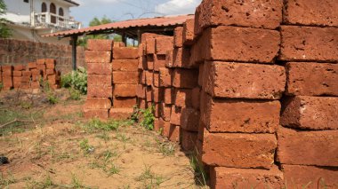 Bahçede yığınla tuğla var. Güneşli bir günde kumlu zeminde çimlerle kaplı eski püskü kırmızı tuğlalar.