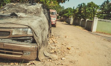 Şehir caddesinde kırık bir araba. Paslı hasarlı araba kirli kumaşla kaplı ve güneşli bir günde eski püskü bir yola park edilmiş.