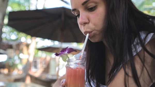 Женщина пьет коктейль в кафе. Взрослая женщина, потягивающая свежие фруктовые напитки через солому, сидя за столом в уличном ресторане в солнечный день — стоковое фото