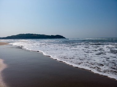 Kıyıda köpüklü deniz dalgaları. Güneşli bir günde ıslak kumlu sahilde süzülen köpüklü deniz suyu dalgaları.