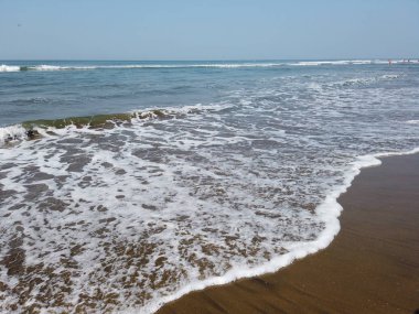 Kıyıda köpüklü deniz dalgaları. Güneşli bir günde ıslak kumlu sahilde süzülen köpüklü deniz suyu dalgaları.