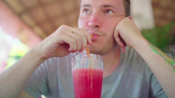 Kafede kokteyl içen bir adam. Yetişkin adam, güneşli bir günde sokak restoranındaki masada otururken samandan taze meyve içeceği yudumluyor. — Stok video