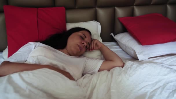 Una hermosa joven se despierta en una cama grande . — Vídeos de Stock