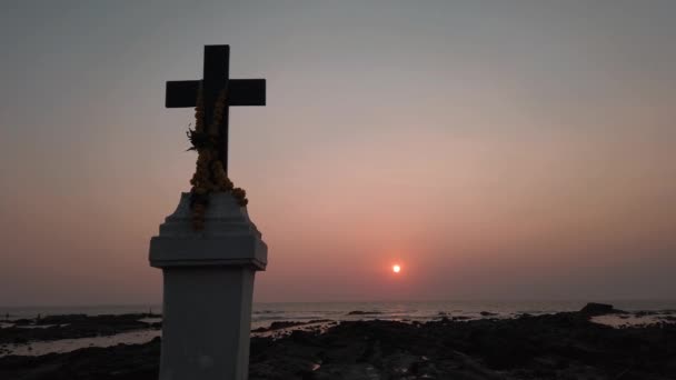 Chrześcijański krzyż na skałach nad morzem przed zachodem słońca. — Wideo stockowe
