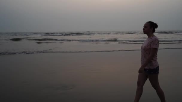日没時にビーチを歩く若い女性は — ストック動画