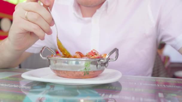 A young man is eating an Indian meat dish in a tropical cafe. — Stock Video