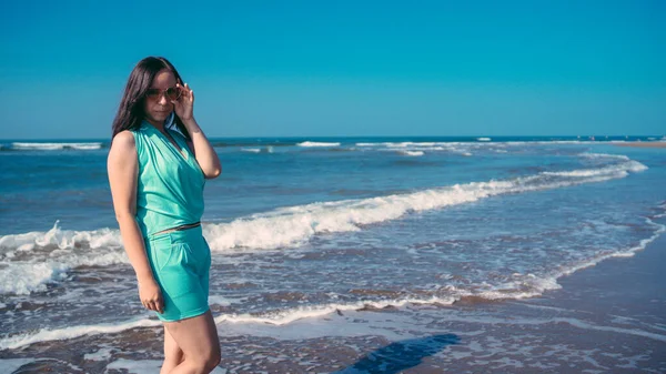 Femme élégante près de la mer. Femme adulte en tenue d'été tendance souriant et regardant la caméra tout en se tenant contre la mer ondulante et le ciel bleu sans nuages sur la station — Photo