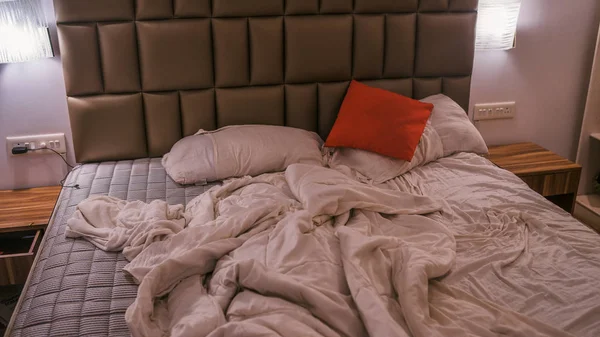 Несделанная кровать в современной спальне. Сверху теплое одеяло и мягкие подушки помещены на удобную невыложенную кровать в стильной современной спальне — стоковое фото