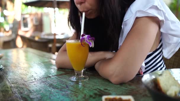 カフェでカクテルを飲む女性。晴れた日にストリートレストランのテーブルに座っている間にわらを介して新鮮な果物飲料をすすります大人の女性 — ストック動画