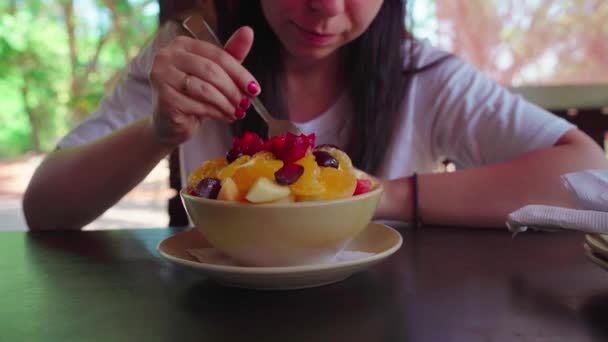 Een vrouw die een exotisch gerecht probeert in een café. Volwassen dame neemt stuk fruit van bord en kauwen voedsel tijdens het rusten in straat restaurant. — Stockvideo
