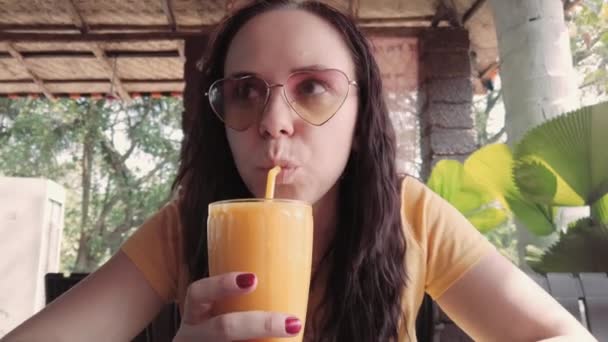 Μια γυναίκα πίνει κοκτέιλ στο καφέ. Ενηλίκων κυρία πίνοντας φρέσκα φρούτα ποτό μέσα από άχυρο, ενώ κάθεται στο τραπέζι στο δρόμο εστιατόριο την ηλιόλουστη μέρα — Αρχείο Βίντεο