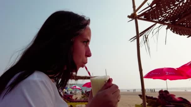 Femme buvant un cocktail au café de la plage. Une dame adulte sirotant une boisson de fruits frais dans la paille, assise sur un lit de soleil dans la cafétéria de la rue par une journée ensoleillée. — Video