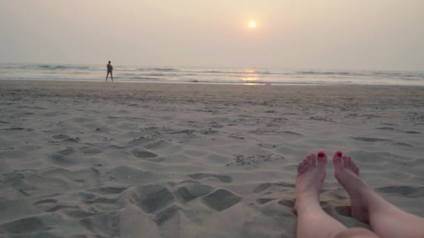 Női láb piros pedikűr fekszik a homokos tengerparton a tenger ellen naplemente. — Stock videók