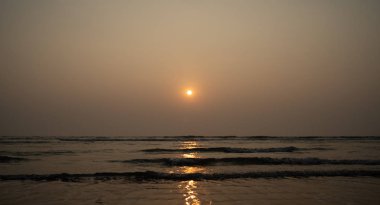 Sunset over sea and beach. Cloudless sundown sky over waving sea and sandy beach in evening on resort