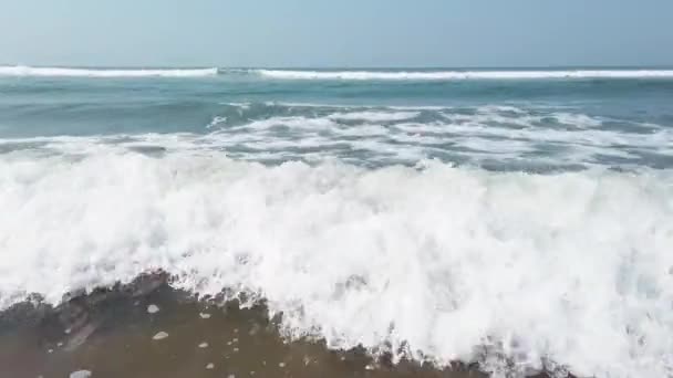 Vagues mousseuses d'eau de mer propre roulant sur une plage de sable mouillé par une journée ensoleillée sur la station balnéaire