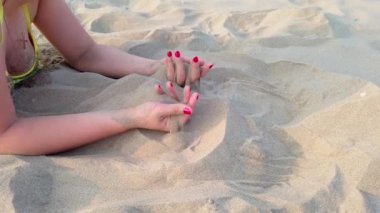 Kadınların elleri avucunun içinde kum topluyor. Kumlu sahilde kumlar elinden düşüyor..