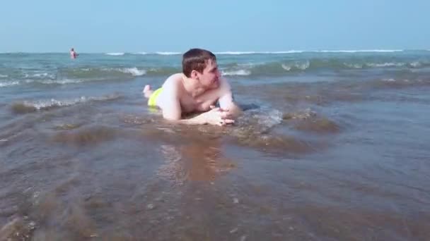 Beau homme éclaboussant dans l'eau. Homme adulte allongé sur le bord de l'océan et baigné par les vagues. — Video