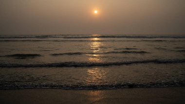 Sunset over sea and beach. Cloudless sundown sky over waving sea and sandy beach in evening on resort