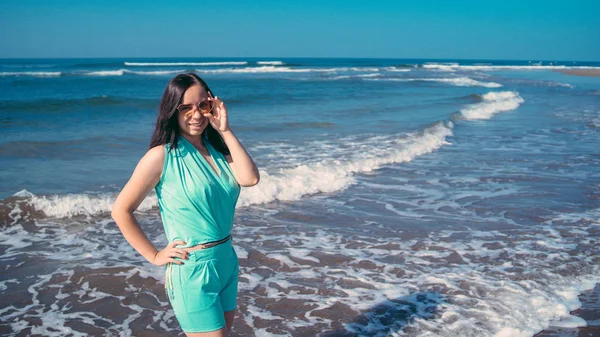 Mulher elegante perto do mar acenando. Mulher adulta em roupa de verão na moda sorrindo e olhando para a câmera enquanto está de pé contra o mar ondulando e céu azul sem nuvens no resort — Fotografia de Stock