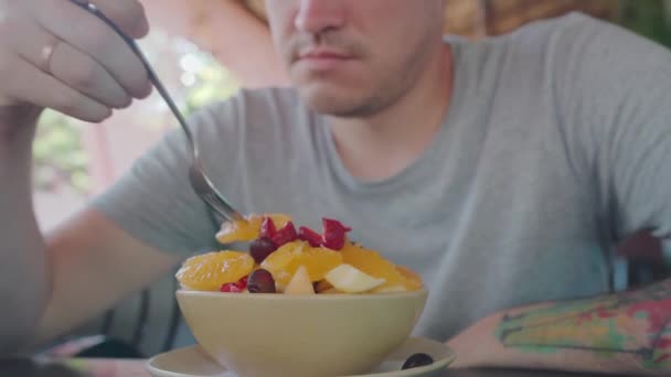 Jeune homme essayant un plat exotique dans la rue café. Adulte prenant un morceau de fruit de l'assiette et mâchant de la nourriture pendant qu'il se repose dans un restaurant de rue. — Video