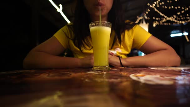女人在咖啡馆里喝鸡尾酒。晚上，一位女士坐在街头餐馆的餐桌旁，一边用稻草喝着新鲜的水果饮料. — 图库视频影像