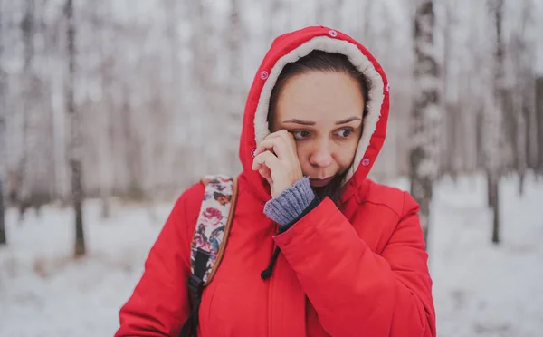 La joven con camisa roja y la campana le frotan los ojos en el bosque de invierno. Cierre. —  Fotos de Stock