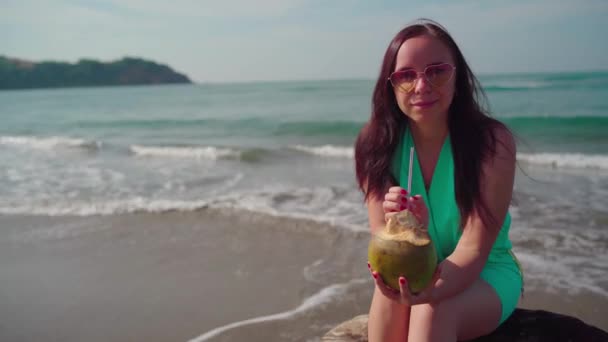 一个美丽的年轻女子在海边或海边喝椰子 — 图库视频影像