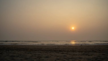 Sunset over sea and beach. Cloudless sundown sky over waving sea and sandy beach in evening on resort