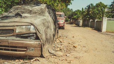 Şehir caddesinde kırık bir araba. Paslı hasarlı araba kirli kumaşla kaplı ve güneşli bir günde eski püskü bir yola park edilmiş.