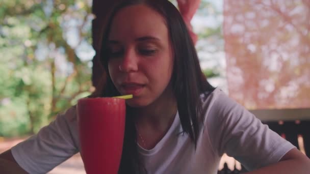 Una mujer bebiendo cóctel en la cafetería. Señora adulta sorbiendo bebida de fruta fresca a través de paja mientras está sentada en la mesa en el restaurante de la calle en un día soleado — Vídeo de stock