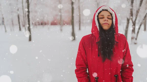 冬の赤いジャケットとフードの若い女性の肖像画。美しい女性は、雪の秋に楽しんで笑顔。ふわふわの雪に包まれて. — ストック写真