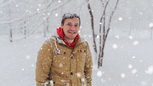 Portrait of young man in jacket in winter season. Handsome man stands and squint in winter park. Fluffy snow envelops everything around. — Stock Photo, Image
