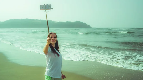 Glückliche Frau beim Selfie in der Nähe des Meeres. Von oben freudige Frau mit Einbeinstativ und Smartphone, um Selfie in der Nähe von winkendem Meer am Strand zu machen — Stockfoto