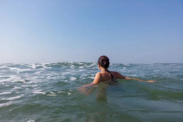 Mujer joven en traje de baño negro pasa tiempo en el mar. Señora adulta nada hacia las olas. — Foto de Stock