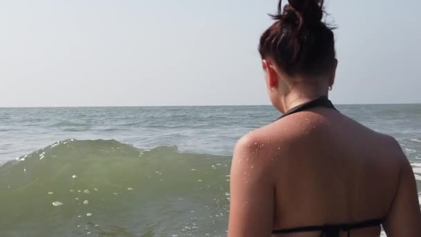 Young woman in black swimsuit spends time in sea. Adult lady swims towards the waves. — Stock Video