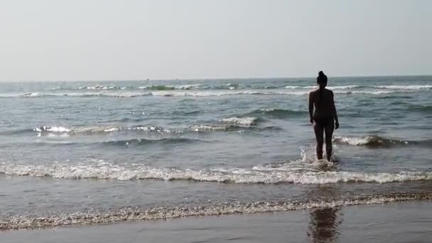 Young woman in black swimsuit spends time in sea. Adult lady swims towards the waves. — Stock Video