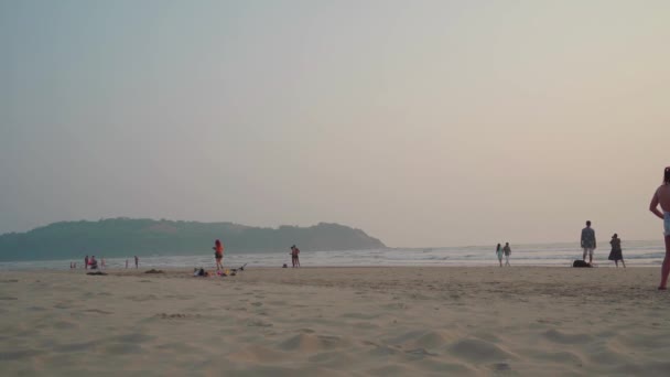 Morjim, Hindistan, 14 Aralık 2019: İnsanlar gün batımında sahilde yürür. Deniz ya da okyanus boyunca bir şerit konsepti. — Stok video