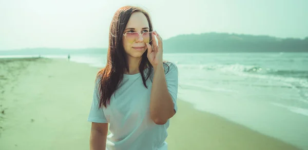 Жінка-туристка позує біля моря. Красива жінка в сонцезахисних окулярах дивиться геть, стоячи на піщаному пляжі біля махаючого моря . — стокове фото