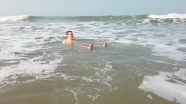 Suda su sıçratan yakışıklı adam. Yetişkin bir adam okyanus kıyısında yatıyor ve deniz dalgalarıyla yıkanıyor..